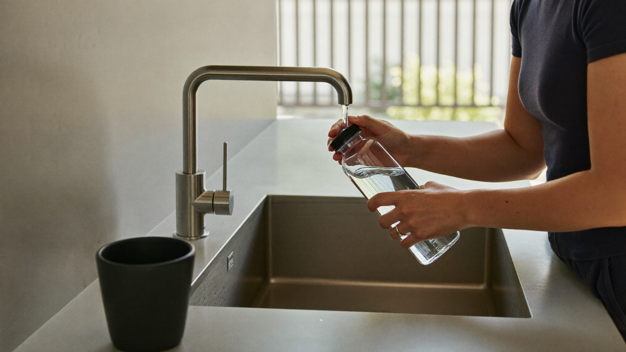 Office employee refilling a reusable water bottle at a kitchen tap
