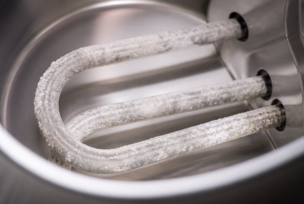 White limescale crust built up on the metal heating elements inside a kettle, showing the effect of hard water